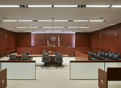 an empty courtroom with chairs and desks in the foreground, two flags on the wall