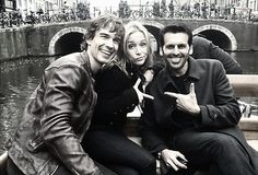 two men and a woman sitting on the back of a boat in front of a canal