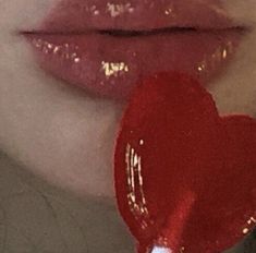 a woman's lips are painted red with gold glitters and the lip is holding a heart shaped lollipop