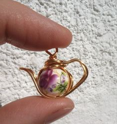 a hand holding a tiny teapot with flowers on it