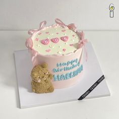 a teddy bear sitting next to a birthday cake on top of a white tablecloth