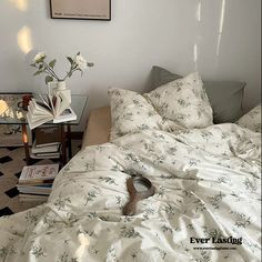 an unmade bed with white sheets and flowers on the pillow, next to a coffee table