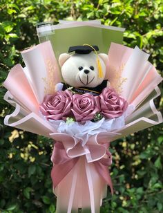 a teddy bear in a graduation cap with pink roses and greenery behind it,