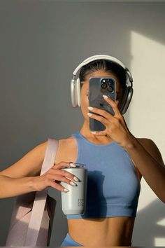 a woman with headphones holding a cup and cell phone in front of her face