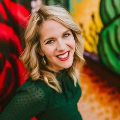 a woman with blonde hair smiling in front of a colorful wall and red flowered background