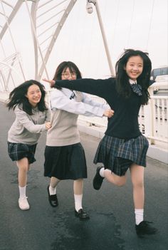 three girls are posing for the camera in front of a bridge and one girl is holding her arms out