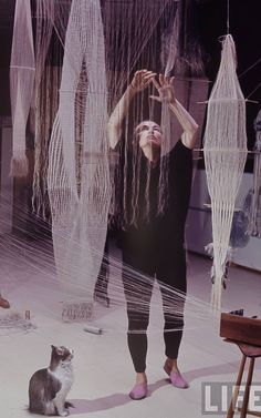 a woman standing next to a cat on top of a floor covered in white yarn