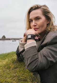 a woman sitting in the grass with her hand on her chin looking at the camera