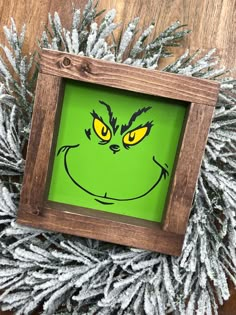 the grin face is drawn on a green background in a wooden frame surrounded by pine branches