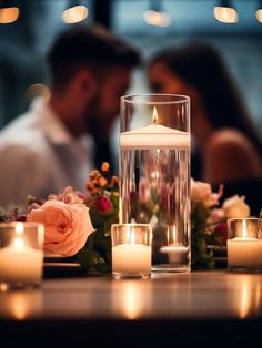 a couple sitting at a table with candles in front of them and flowers on the table