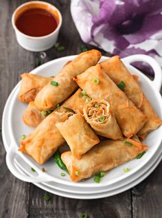 a white plate topped with vegetable spring rolls next to a cup of tea and sauce