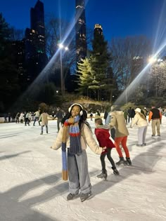 people skating on an ice rink at night with lights shining in the background and skyscrapers