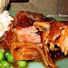 a green plate topped with meat and rice covered in gravy next to peas