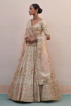 a woman in a white and gold bridal gown standing next to a wall with her hands on her hips