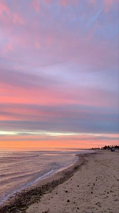 the sky is pink and purple as the sun sets on the beach with footprints in the sand