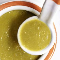 a white bowl filled with green soup on top of a orange and white striped plate