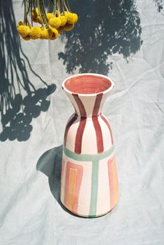 a vase sitting on top of a table next to some yellow and green flowers hanging from the ceiling