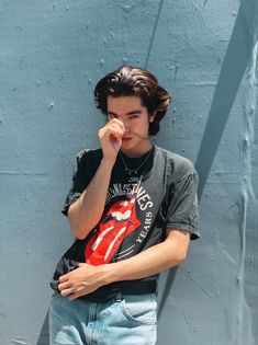 a young man leaning against a blue wall with his hand on his face and looking at the camera