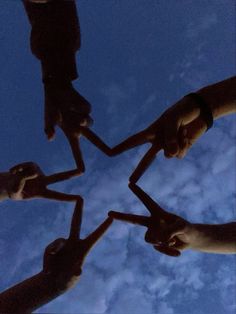 four people holding their hands together in the shape of a star against a blue sky