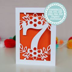 an orange and white greeting card with the number seven on it, surrounded by pom poms