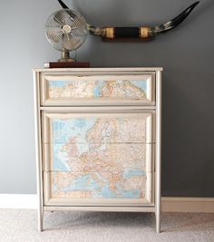 a white dresser with a map on it and a fan mounted to the wall behind it