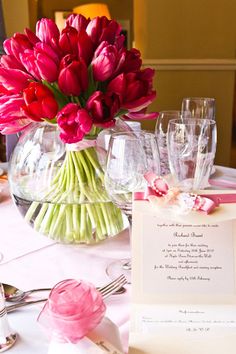 there is a vase filled with flowers and wine glasses next to a card on the table