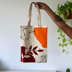 a person holding up a bag with an orange and red design on it, in front of a white wall