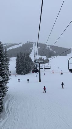 several people skiing down a snow covered slope under a ski lift with trees in the background