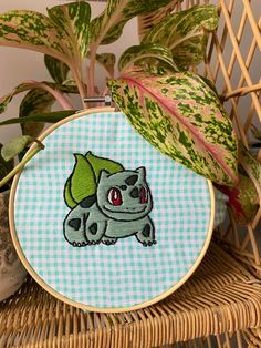 a close up of a embroidery on a basket near a potted plant with a green leaf