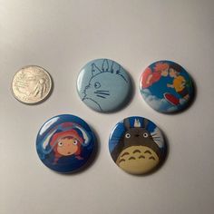 four buttons with different characters on them sitting next to one another and a coin in the background