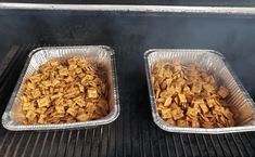 two metal trays filled with food cooking on top of an open grill