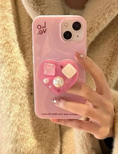 a woman holding a pink phone case with pearls and hearts on the back, in front of a fur coat