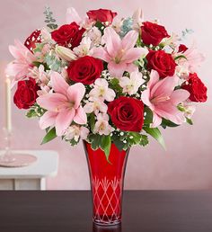 a vase filled with lots of pink and red flowers on top of a wooden table