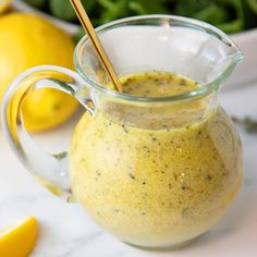 a glass pitcher filled with yellow liquid next to lemons and spinach in the background