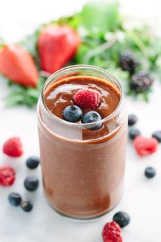 a glass jar filled with chocolate pudding and berries on top of a white table next to strawberries