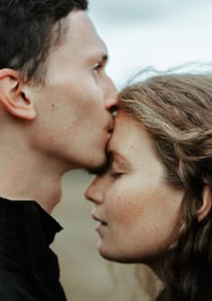 a man and woman kissing each other in front of the camera on a cloudy day