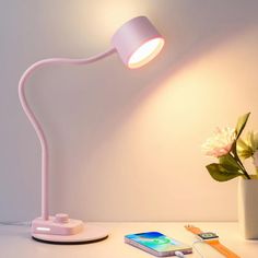 a white table lamp sitting on top of a desk next to a vase with flowers