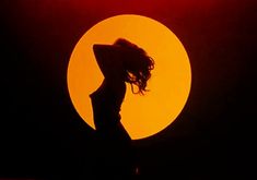 the silhouette of a woman wearing a hat in front of a yellow and red sun