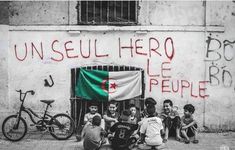 children sitting on the ground in front of a wall with graffiti