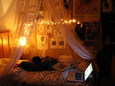 a person laying in bed with a laptop on their lap and lights strung from the ceiling