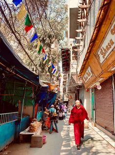 a woman in a red robe walking down a street next to buildings and flags hanging from the ceiling