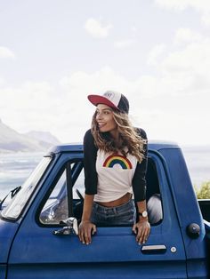 a woman standing in the back of a blue truck with a rainbow on her shirt