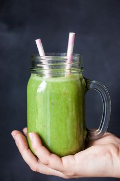 a person holding a green smoothie in a mason jar with two straws sticking out of it