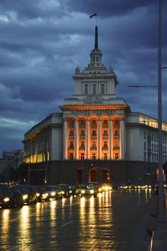 a large building lit up at night with lights on it's sides and cars parked in front