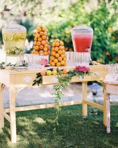 a table topped with oranges and drinks on top of green grass covered field next to trees