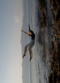 a woman is jumping in the air near the ocean