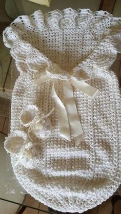 a crocheted baby blanket with a bow on the front and back, sitting on top of a tile floor