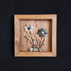 a wooden frame with rocks and flowers in it on a black background, as seen from above