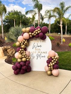 a sign with balloons attached to it in front of some palm trees and bushes on the sidewalk