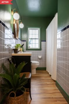 a bathroom with green walls and white tiles on the walls, along with a plant in a basket